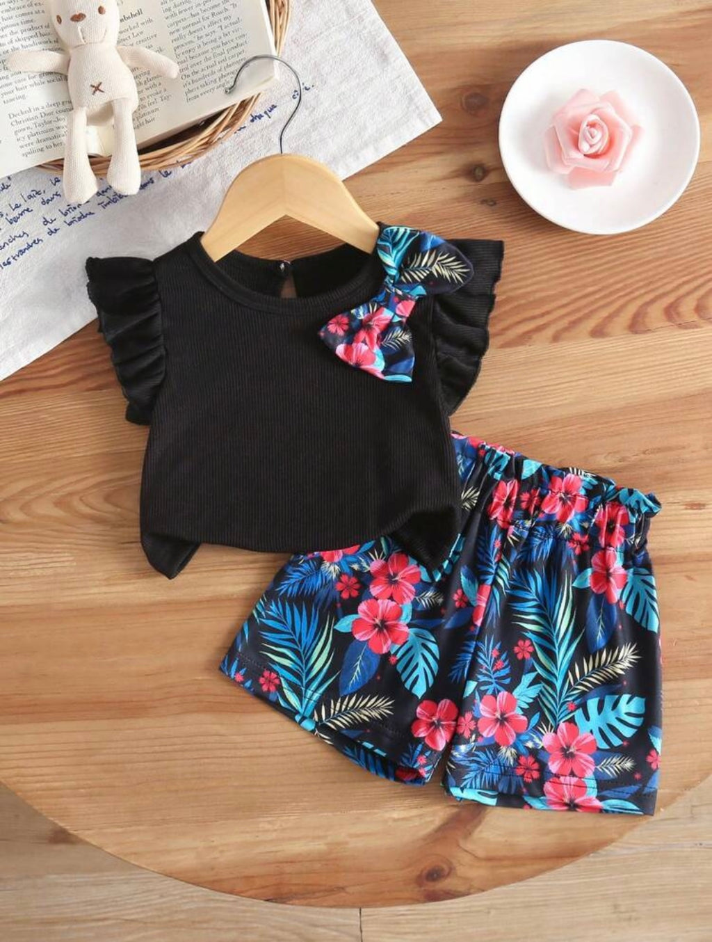 Black top with floral ruffled sleeves and matching shorts on a wooden surface.