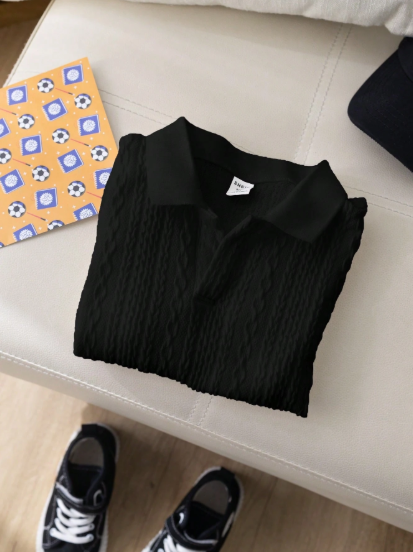 Black polo shirt with a brand logo on a white surface, with sneakers partially visible at the bottom.